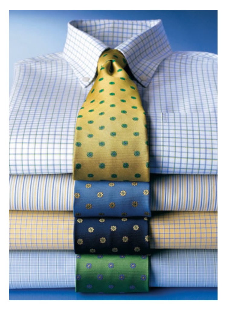 A stack of freshly pressed folded dress shirts with silk neckties laid across them